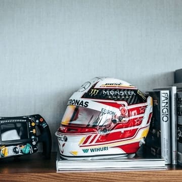 A foto of many different f1 themed products being displayed in a shelve. Products being shown for sale on GPBox with a steering wheel, a helmet and f1 themed book.